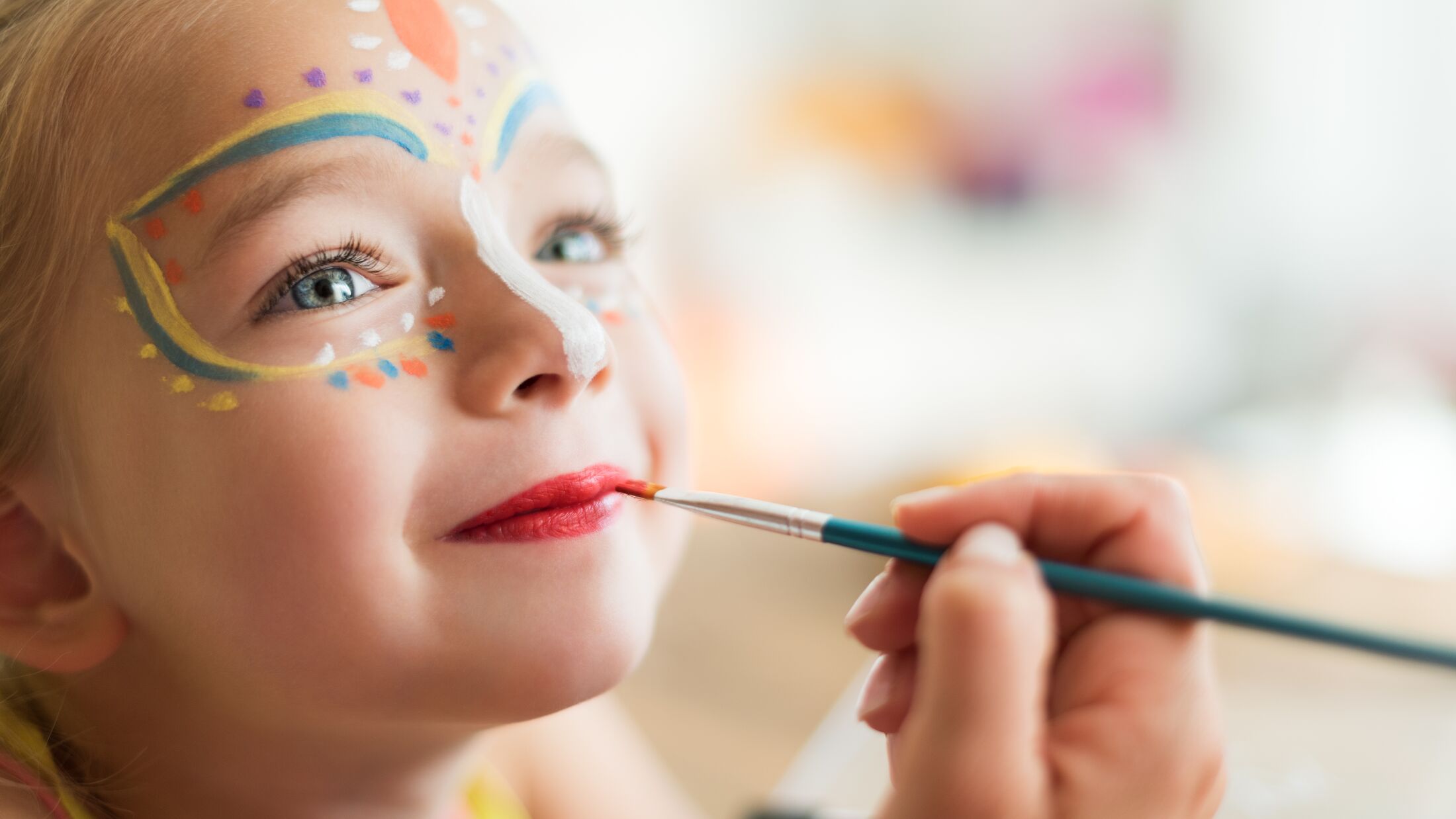 Cute little girl having her face painted for Halloween party. Halloween or carnival family lifestyle background. Face painting, headshot close up.